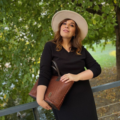 Mulher com vestido preto, chapéu bege e bolsa castanha exterior