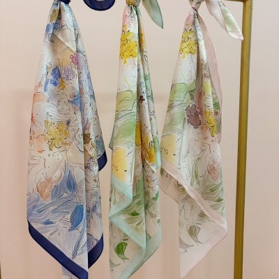 Três lenços de tecido leve com padrão floral e bordas coloridas pendurados num cabide.