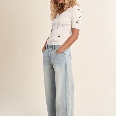 Mulher vestida com camisola branca bordada, jeans largos azuis claros e sapatos bege.