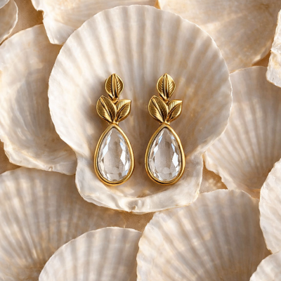 Brincos dourados com pedras transparentes sobre conchas brancas
