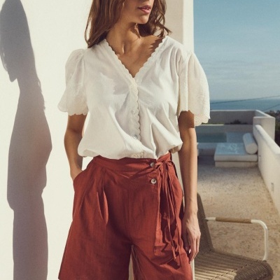 Conjunto feminino com blusa branca e calção terracota ao ar livre numa varanda
