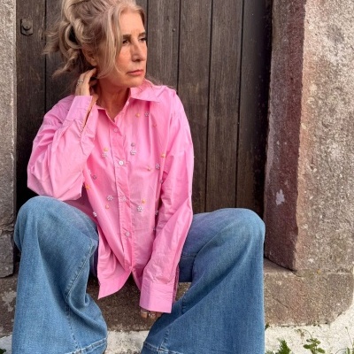 Mulher com camisa rosa bordada e calças de ganga largas sentada em degrau de pedra