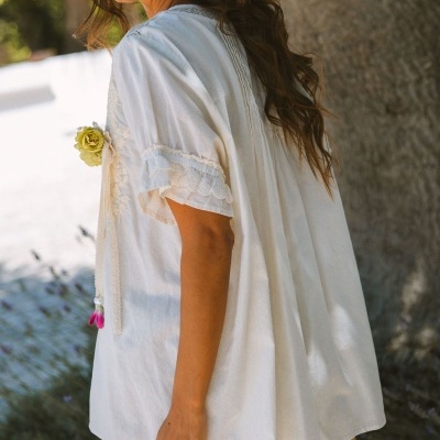 Blusa branca feminina com detalhes de renda e mangas curtas ao ar livre.
