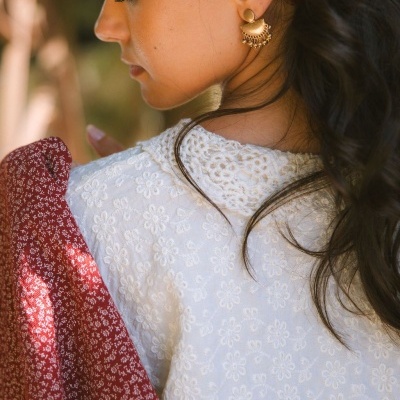 Mulher com vestido branco bordado e brinco dourado, com lenço vermelho no cabelo.