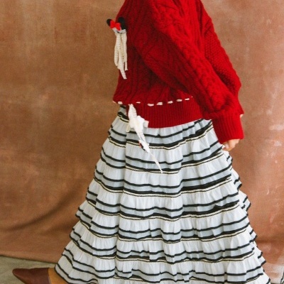 Mulher a usar camisola vermelha de malha e saia branca riscada preta com sapatos castanhos