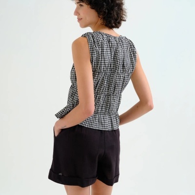 Modelo de costas com blusa quadriculada preta e branca sem mangas e calções pretos.