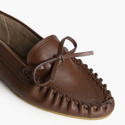 Mocassim castanho em pele com laço franjado e costura visível.