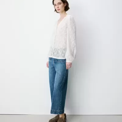 Mulher com blusa branca rendada, calças de ganga azuis e sapatos castanhos