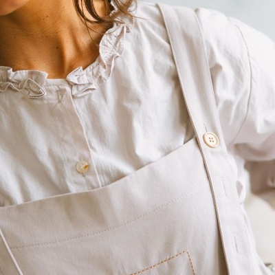 Blusa branca com gola franzida e jardineira bege com bordado de flor.
