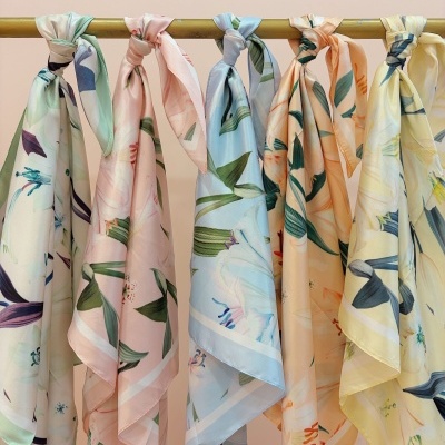Seis lenços de padrão floral em cores pastel pendurados numa barra metálica dourada.