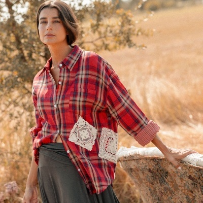 Mulher com camisa xadrez vermelha com rendas brancas e saia cinzenta num campo seco ao ar livre
