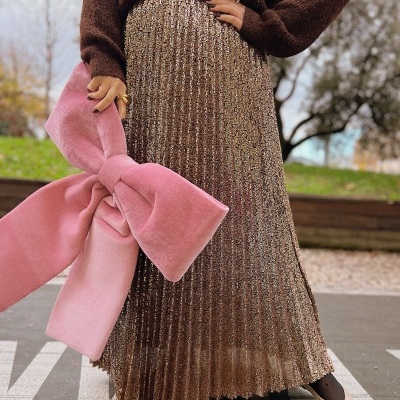 Conjunto com saia longa brilhante castanha dourada, suéter castanho, bolsa rosa com laço e sapatos bege com pérolas