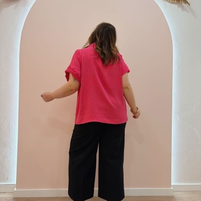 Mulher de costas com blusa rosa, calças pretas largas e botas camel de salto em cenário decorativo.