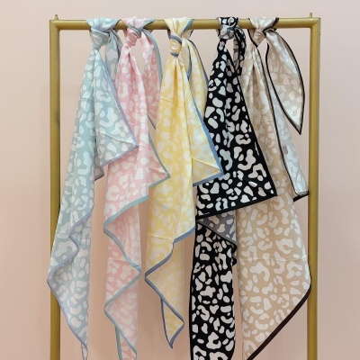 Cinco lenços pendurados em cabide dourado com padrão de manchas coloridas