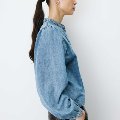 Blusa de ganga azul com botões e calças castanhas trançadas vista de perfil.