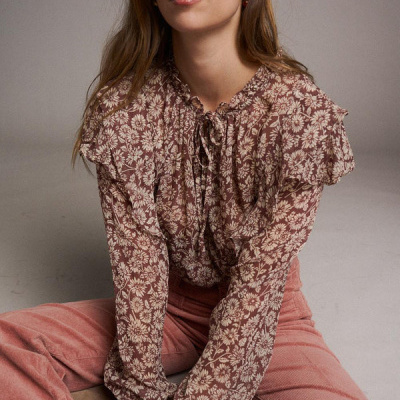 Mulher sentada com blusa floral castanha e calças rosa em veludo cotelê