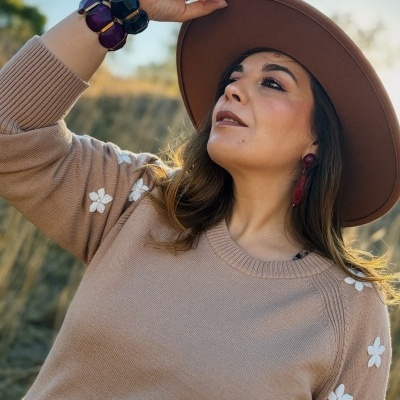 Mulher com camisola bege com flores brancas nas mangas e chapéu castanho em ambiente natural