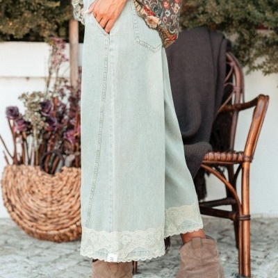 Calças de ganga azul clara com renda, botas castanhas, blusa floral, cadeira e cesta de vime