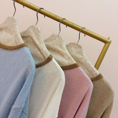 Quatro camisolas de malha em azul, creme, rosa e bege com decote dourado penduradas em cabides florais numa barra metálica amarela