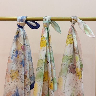 Três lenços de seda com padrões florais pendurados numa barra metálica