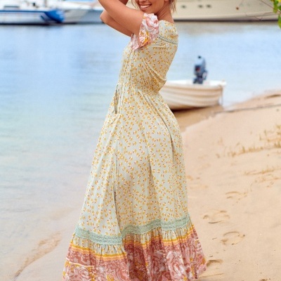 Mulher com vestido longo floral na praia, barcos ao fundo