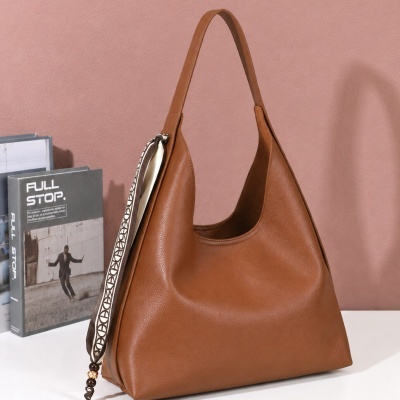 Mala castanha de mão com fita decorativa pendurada e livros ao fundo sobre mesa branca