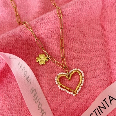 Colar dourado com pendente de coração e trevo sobre fundo rosa
