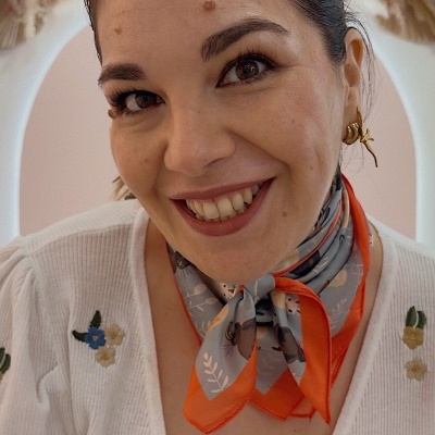Mulher com lenço floral cinza e laranja ao pescoço e blusa branca bordada com flores