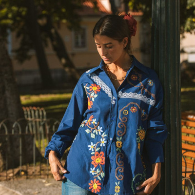 Mulher com camisa azul bordada de manga comprida ao ar livre perto de poste verde