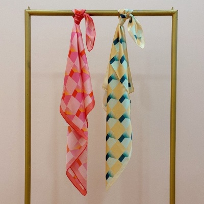 Dois lenços de seda com padrões geométricos pendurados em cabide dourado