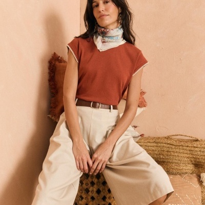 Mulher de camiseta terracota e calças bege sentada com lenço e acessórios