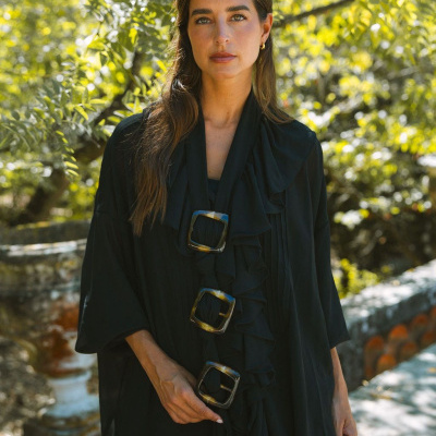 Poncho preto com fivelas em padrão tartaruga usado por mulher ao ar livre