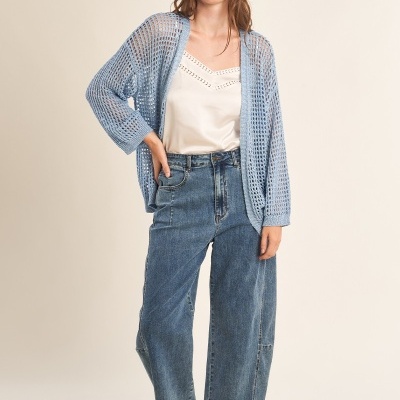 Mulher com camisola branca, cardigan azul e jeans largos com sandálias castanhas