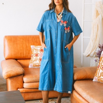 Vestido midi de ganga azul com borboletas vermelhas, mulher em sala com sofá castanho.