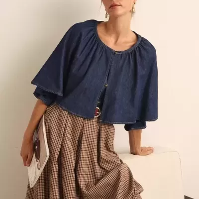 Mulher com casaco azul de ganga e saia xadrez castanha sentada num sofá creme