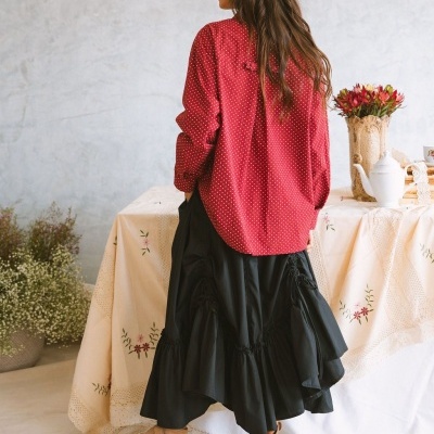 Mulher veste blusa vermelha de pontos brancos, saia preta larga e botas castanhas junto a mesa decorada