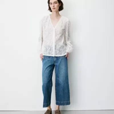 Blusa branca de renda com mangas compridas, jeans azuis largos e sapatos castanhos