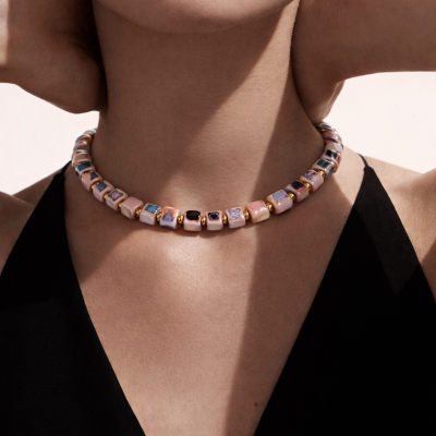 Colar de contas quadradas multicoloridas em tons pastel com espaçadores dourados no pescoço de uma mulher com top preto.