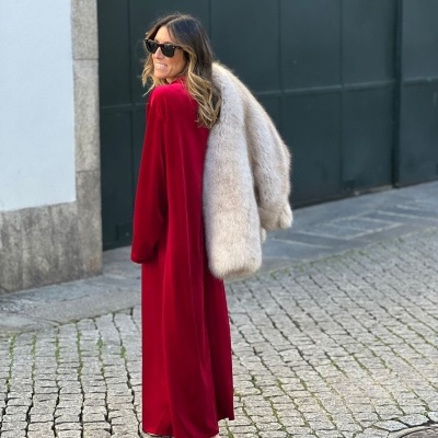 Mulher de vestido longo vermelho e casaco de pelo bege com óculos escuros numa rua de calçada