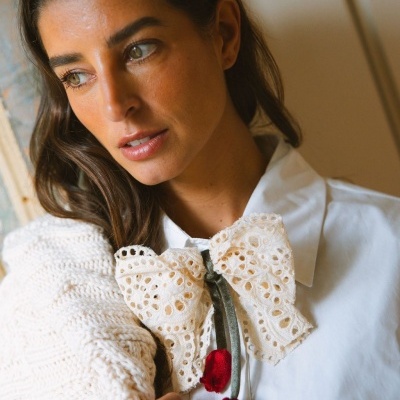 Laço de renda branca com laços vermelhos numa camisa branca e suéter creme