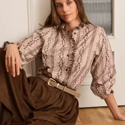 Camisa floral castanha e bege com saia castanha e cinto bege sentada em chão de madeira