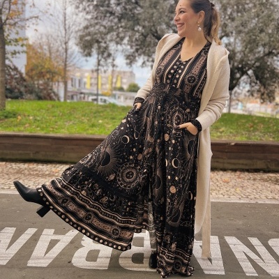 Mulher vestindo vestido longo preto com padrão espacial bege, casaco bege e botas pretas ao ar livre