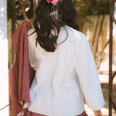 Camisola branca manga comprida padrão floral relevo, lenço vermelho cabeça, saia vermelha padrão branco, vista de costas.