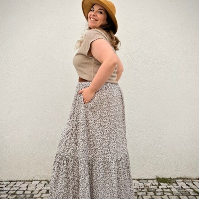 Mulher com chapéu castanho, camisa beige e saia com padrão de leopardo