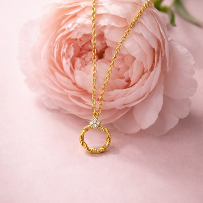 Colar dourado com pendente circular e pequenos cristais sobre flor rosa