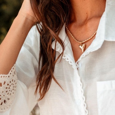 Colar dourado com pendente de coração na mulher com camisa branca rendada