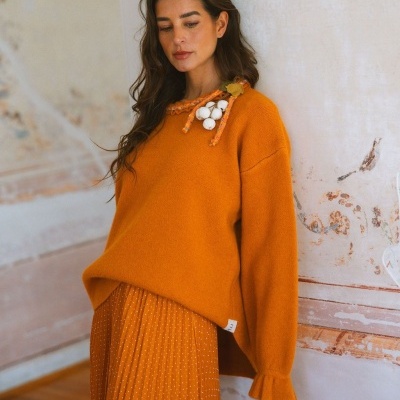 Mulher com camisola de malha laranja e saia plissada laranja com pontos brancos