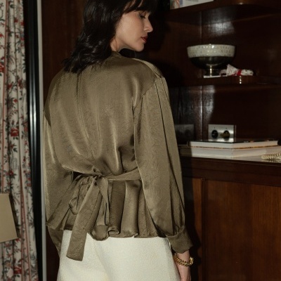 Mulher com blusa verde-oliva e calções creme junto a estante de madeira