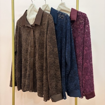 Três camisas de renda castanha, azul escuro e bordeaux penduradas num cabide amarelo em fundo neutro
