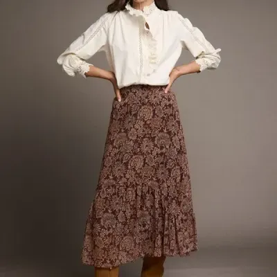 Mulher com blusa branca rendada, saia floral castanha e botas castanhas